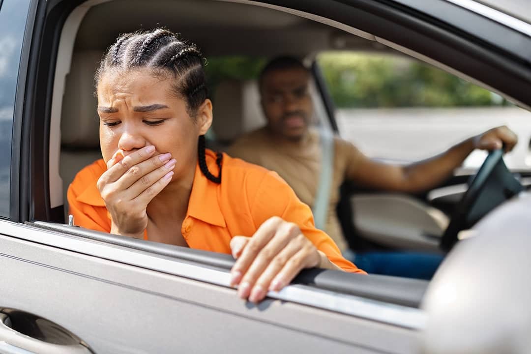 A person feeling nauseous and leaning out of the car's window during a quick stop.